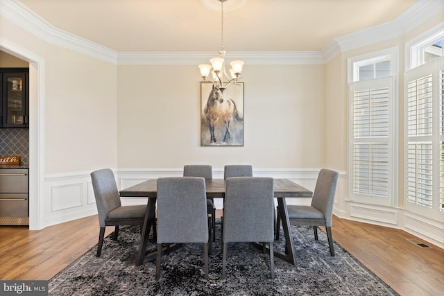 dining room with an inviting chandelier, visible vents, ornamental molding, and wood finished floors