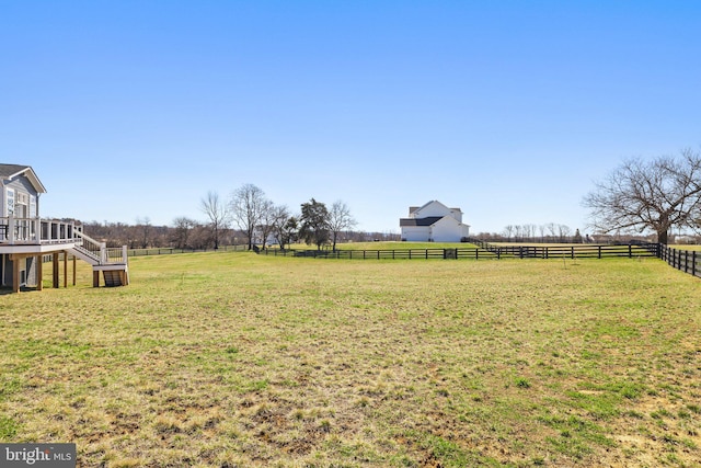 view of yard featuring a deck, a rural view, fence, and stairs