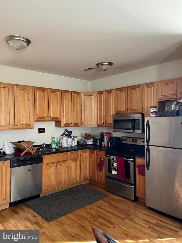 kitchen featuring a sink, stainless steel appliances, light wood-style floors, and brown cabinets