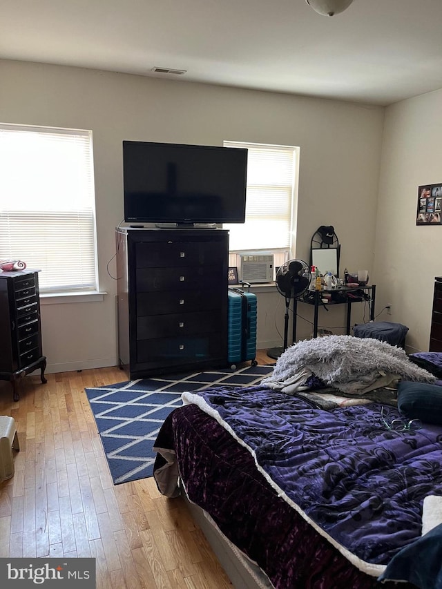 bedroom featuring cooling unit, wood finished floors, multiple windows, and visible vents