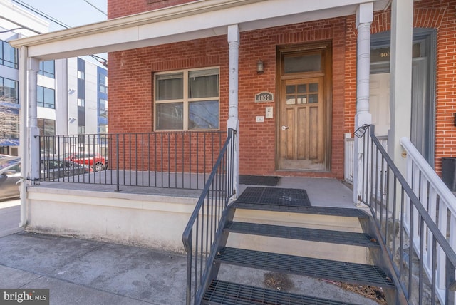 property entrance featuring covered porch and brick siding