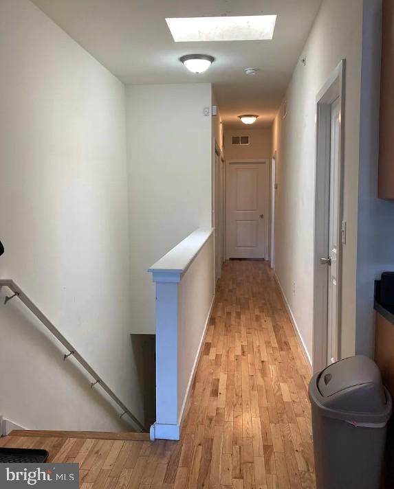 hallway with an upstairs landing, a skylight, light wood finished floors, and visible vents