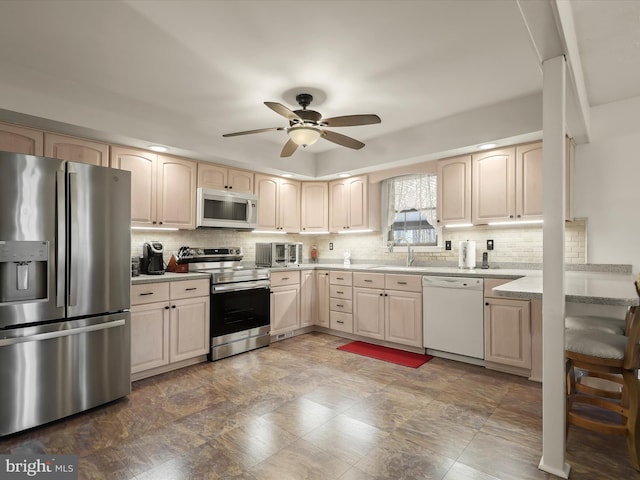 kitchen with stainless steel appliances, ceiling fan, decorative backsplash, and a sink