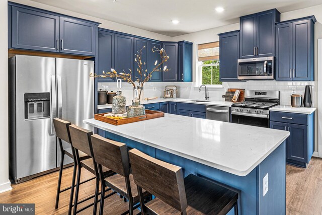 kitchen with light wood-style flooring, a breakfast bar, stainless steel appliances, a sink, and blue cabinets