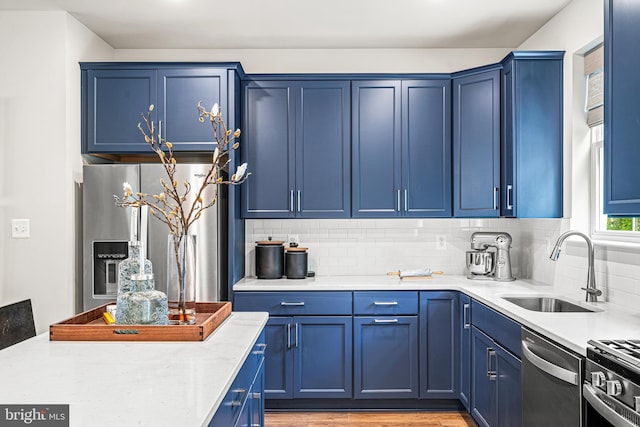kitchen featuring a sink, backsplash, light wood finished floors, appliances with stainless steel finishes, and blue cabinetry