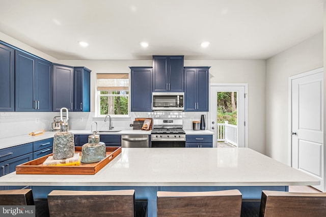 kitchen with decorative backsplash, blue cabinetry, stainless steel appliances, a sink, and a breakfast bar area