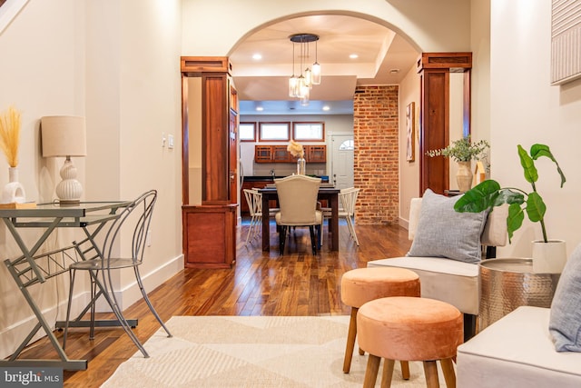 interior space with arched walkways, a tray ceiling, hardwood / wood-style flooring, and baseboards