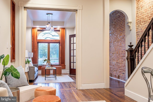 entryway with brick wall, stairway, wood finished floors, and baseboards