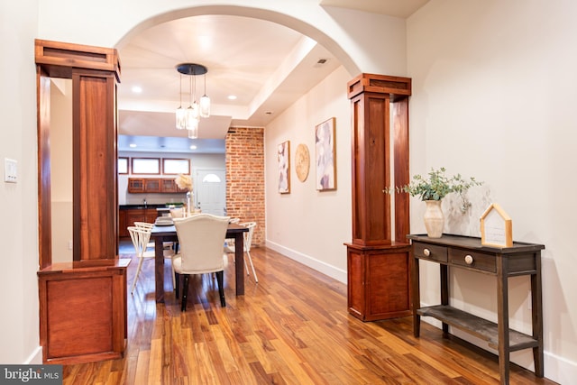 dining room with a raised ceiling, arched walkways, baseboards, and wood finished floors
