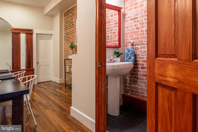 bathroom with baseboards, wood finished floors, and brick wall