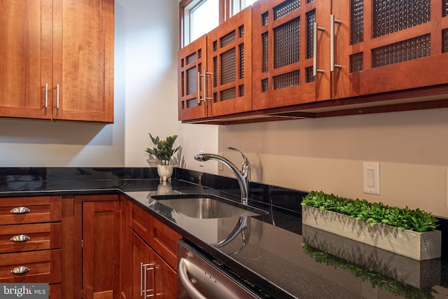 kitchen with dark stone countertops, glass insert cabinets, brown cabinetry, stainless steel dishwasher, and a sink