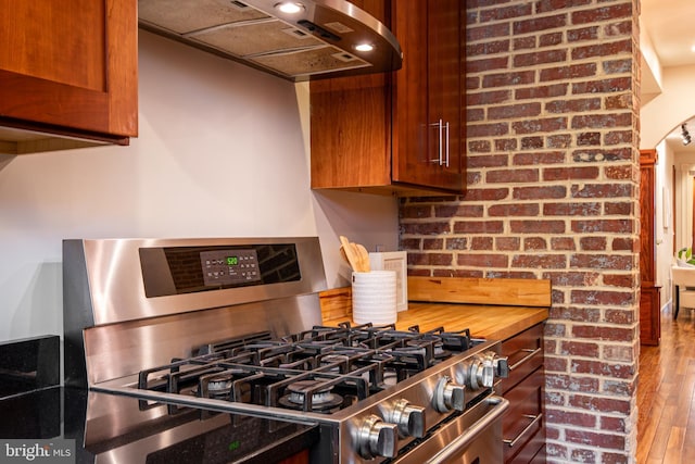 kitchen featuring gas stove, brown cabinets, wood finished floors, and range hood