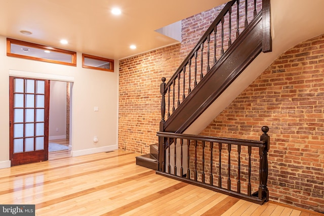 stairs with brick wall, recessed lighting, hardwood / wood-style flooring, and baseboards