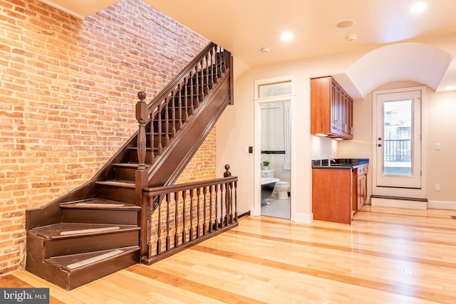 stairs with hardwood / wood-style floors, brick wall, baseboards, and arched walkways