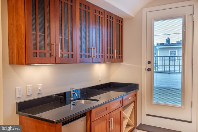 kitchen with brown cabinets, dishwasher, dark countertops, and glass insert cabinets