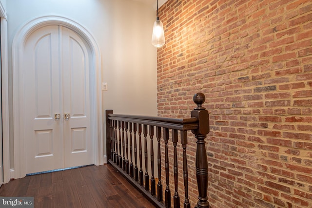 hall featuring dark wood-type flooring, an upstairs landing, and brick wall