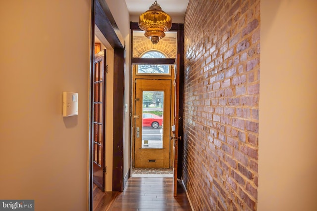 doorway to outside featuring brick wall and dark wood-style flooring