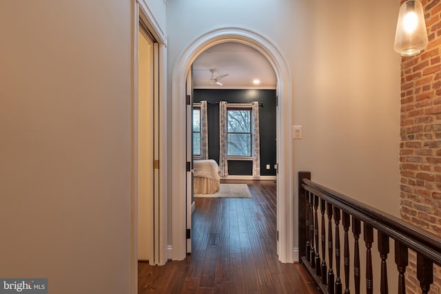 corridor featuring an upstairs landing, arched walkways, and dark wood finished floors