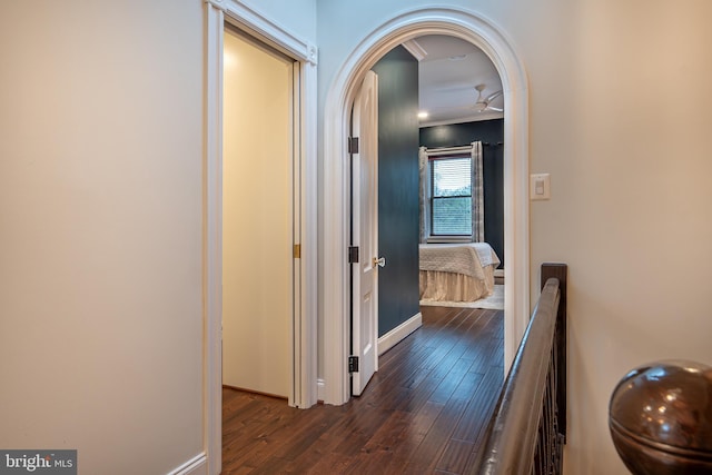 hallway with arched walkways, dark wood-style flooring, and baseboards