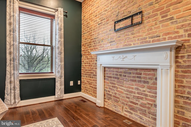interior space featuring brick wall, baseboards, dark wood finished floors, and visible vents