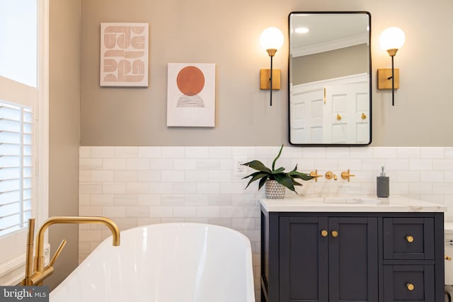 full bathroom featuring a freestanding tub, vanity, ornamental molding, a wainscoted wall, and tile walls