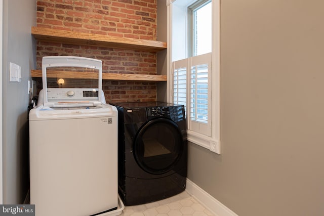 laundry room featuring baseboards, brick wall, washer and clothes dryer, laundry area, and tile patterned floors