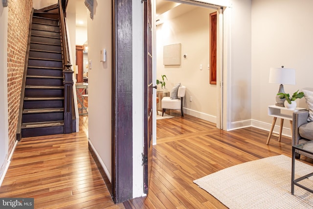 corridor featuring light wood-style floors, brick wall, baseboards, and stairs