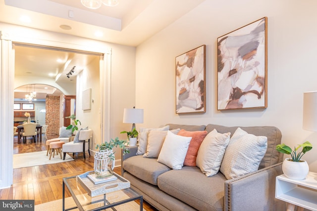 living room featuring wood-type flooring, arched walkways, and an inviting chandelier