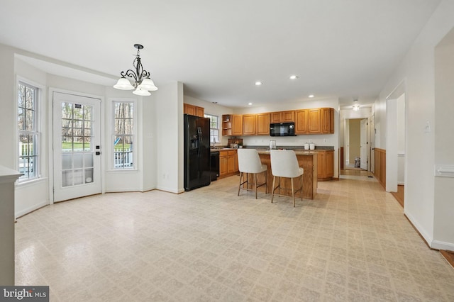 kitchen with black appliances, recessed lighting, a chandelier, a breakfast bar area, and baseboards