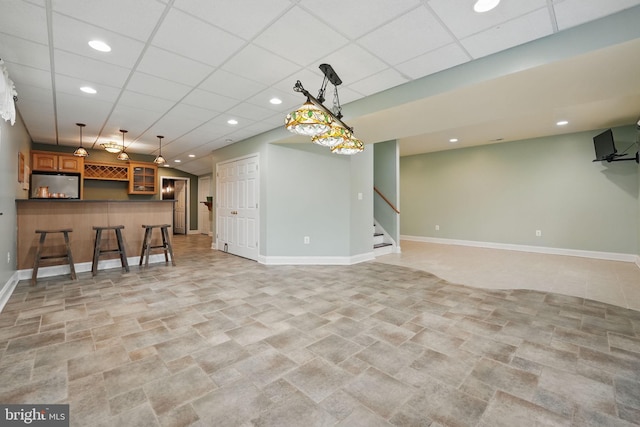 unfurnished living room featuring stairway, a paneled ceiling, baseboards, and a dry bar
