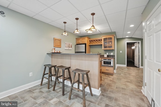 kitchen featuring baseboards, refrigerator, a peninsula, glass insert cabinets, and a breakfast bar area