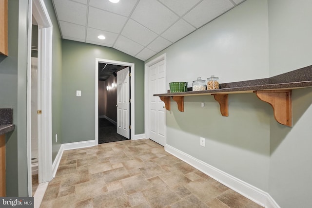 interior space featuring baseboards, dark countertops, a breakfast bar area, stone finish flooring, and a drop ceiling