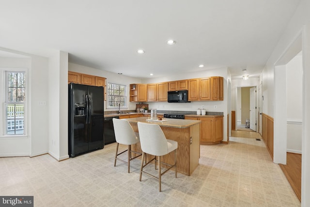 kitchen featuring a breakfast bar, recessed lighting, open shelves, a kitchen island, and black appliances