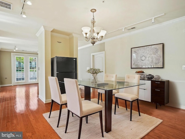 dining area with visible vents, an inviting chandelier, wood finished floors, crown molding, and track lighting