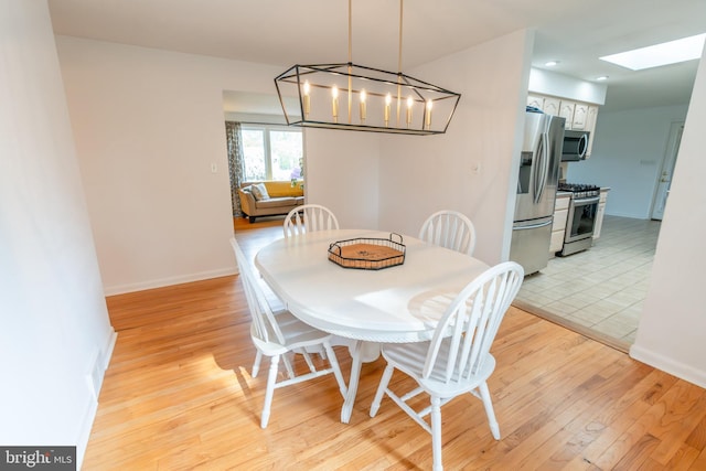dining room with a skylight, an inviting chandelier, baseboards, and light wood finished floors