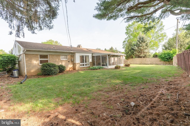 back of house featuring a fenced backyard, a chimney, a sunroom, brick siding, and a yard