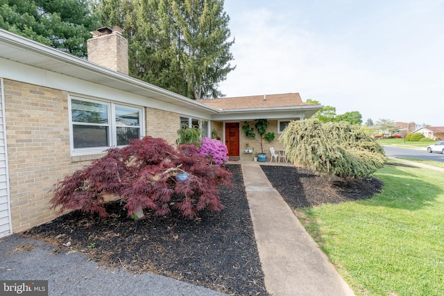 view of front of house with brick siding, a front yard, a chimney, and a porch