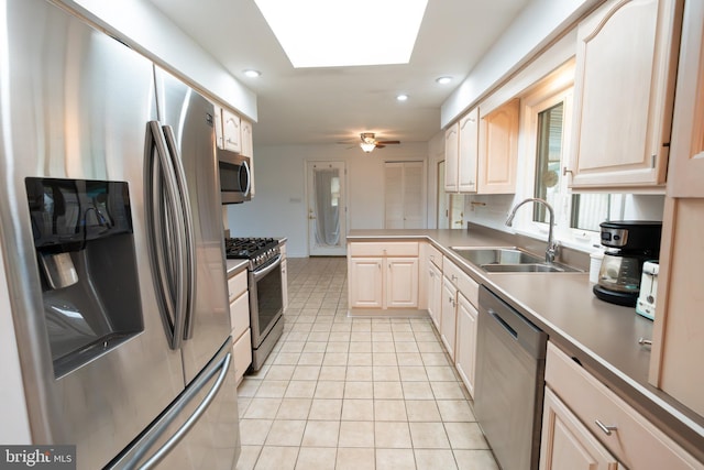 kitchen featuring a peninsula, a sink, light tile patterned floors, a skylight, and stainless steel appliances