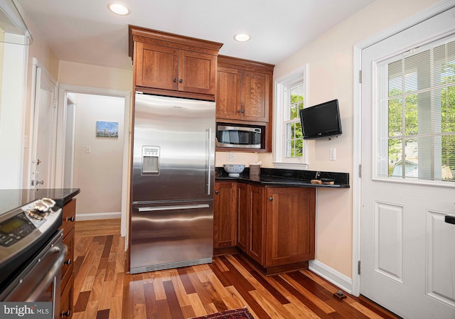 kitchen featuring built in appliances, wood finished floors, baseboards, brown cabinetry, and recessed lighting
