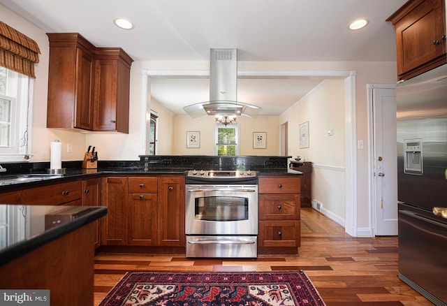 kitchen with stainless steel appliances, island range hood, light wood-type flooring, a sink, and baseboards