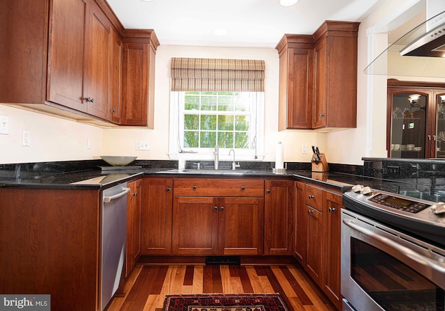 kitchen featuring stainless steel appliances, dark wood-style flooring, brown cabinetry, a sink, and recessed lighting