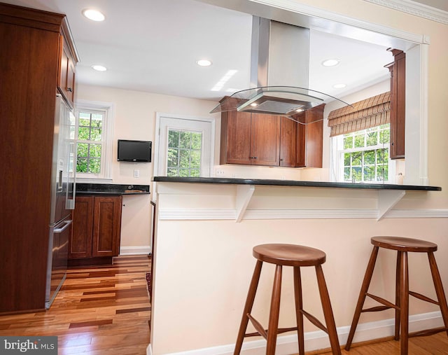 kitchen with light wood-type flooring, built in fridge, island exhaust hood, dark countertops, and recessed lighting