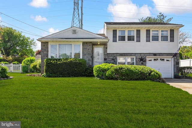 tri-level home featuring a garage, fence, a front lawn, concrete driveway, and stone siding