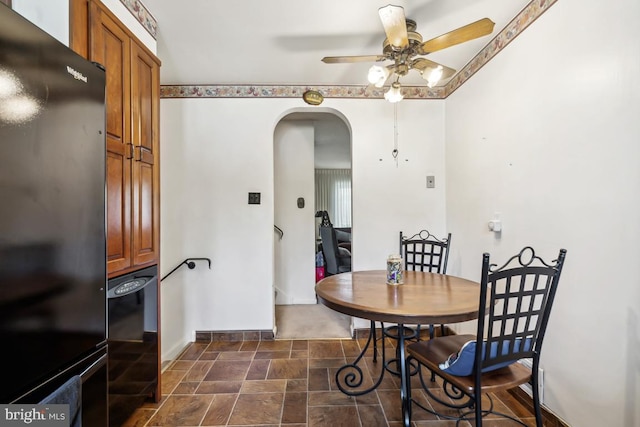 dining area featuring baseboards, arched walkways, stone finish flooring, and a ceiling fan
