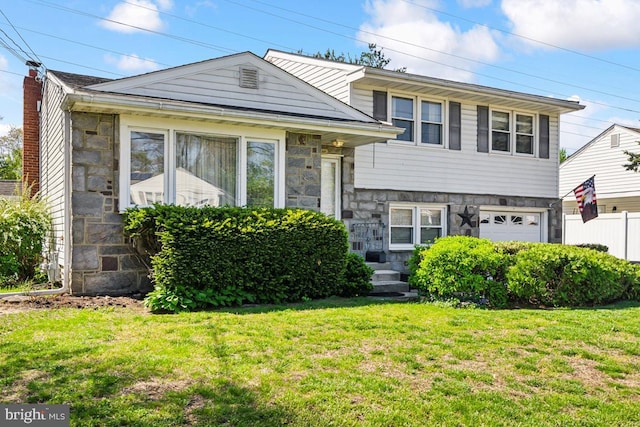 tri-level home featuring fence, an attached garage, a front yard, and stone siding
