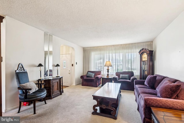 living area featuring arched walkways, baseboards, a textured ceiling, and light colored carpet
