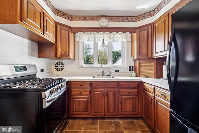 kitchen with freestanding refrigerator, gas range, light countertops, brown cabinets, and a sink