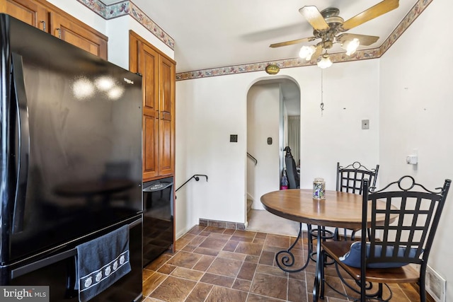 dining space with a ceiling fan, stone finish flooring, visible vents, arched walkways, and baseboards