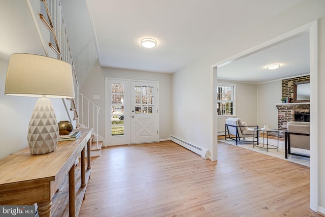 foyer entrance with a baseboard heating unit, stairs, a baseboard radiator, a brick fireplace, and wood finished floors