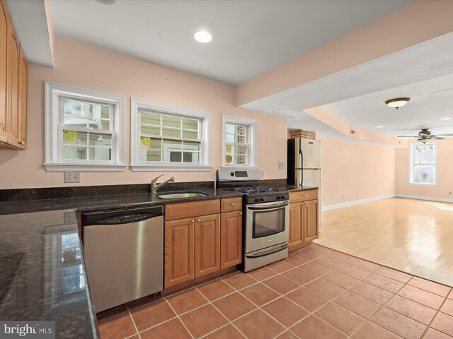 kitchen with open floor plan, tile patterned flooring, stainless steel appliances, dark stone counters, and a sink